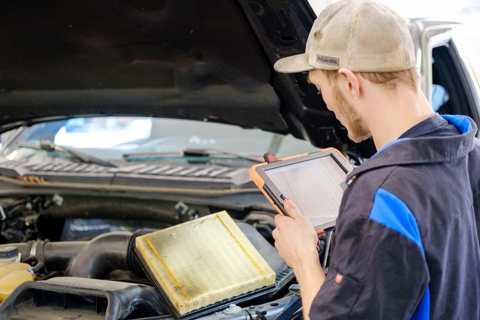 Mechanic using a tablet to diagnose a car engine with the hood open.