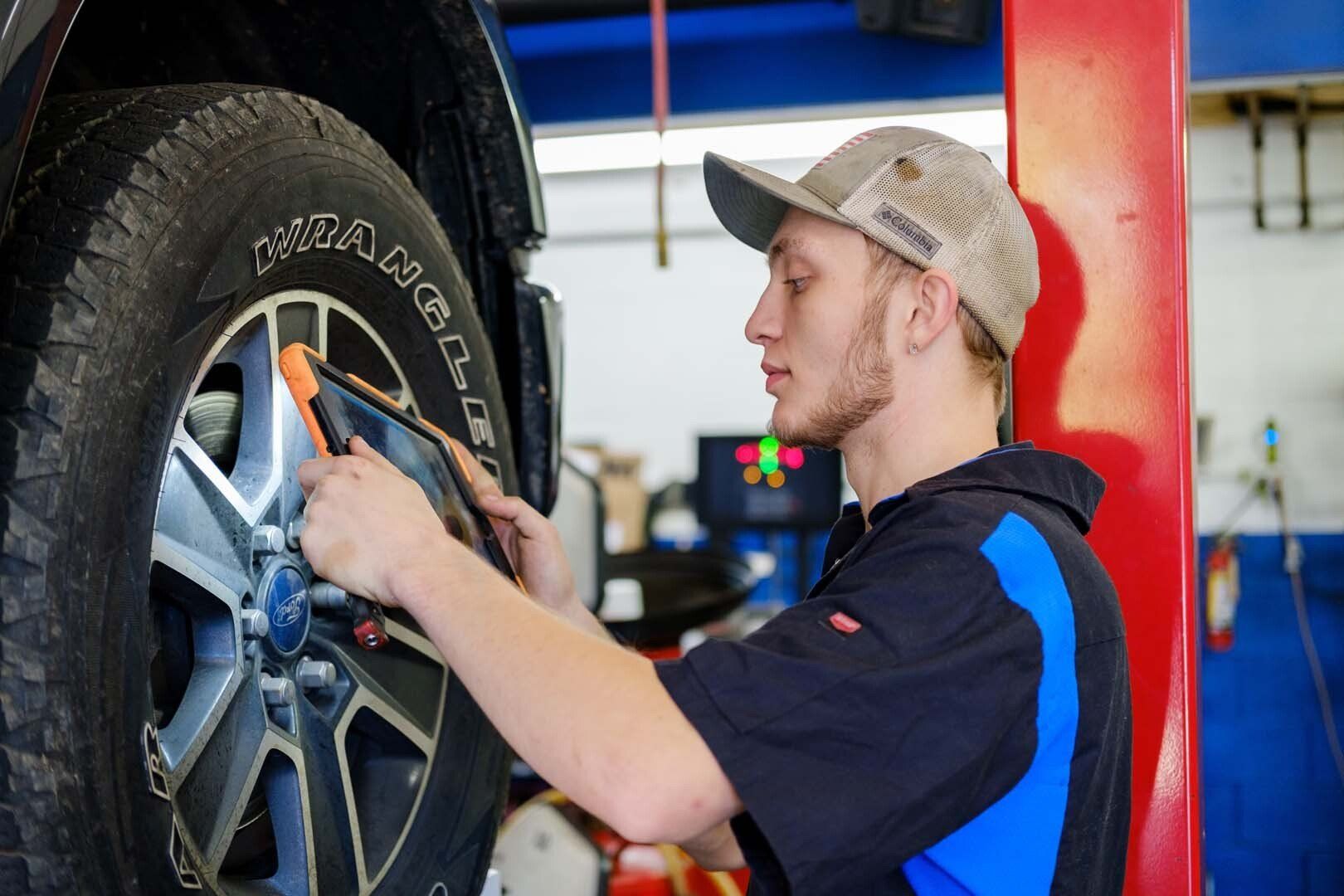 Mechanic using a tablet to inspect a car wheel in a garage.