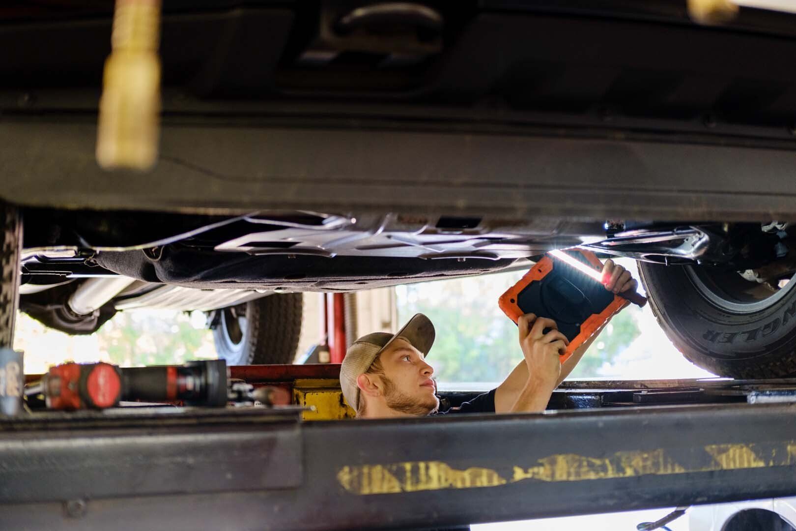 Mechanic uses tablet to inspect car undercarriage on a lift.