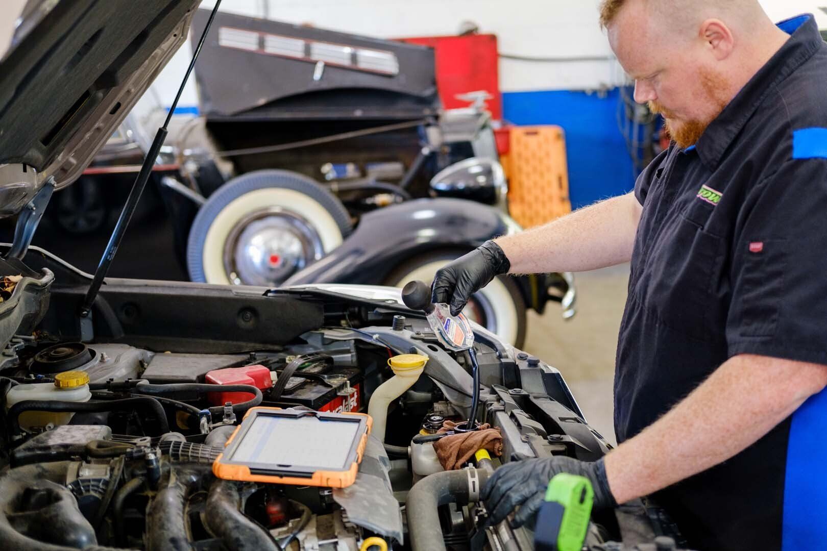 Mechanic working on a car engine in a garage; holding a tool, checking readings.
