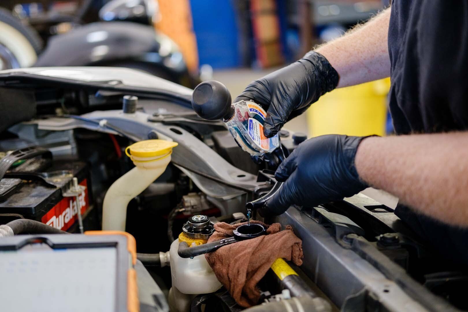 Mechanic in black gloves adding fluid to a car engine in a garage.