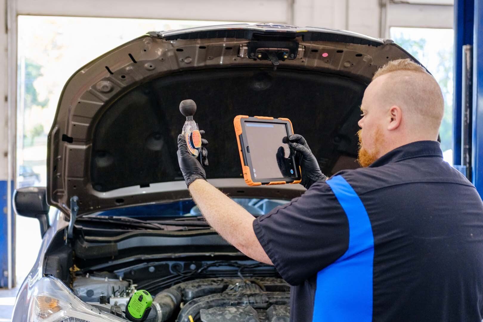 Mechanic with tablet and tool inspecting car engine in garage.