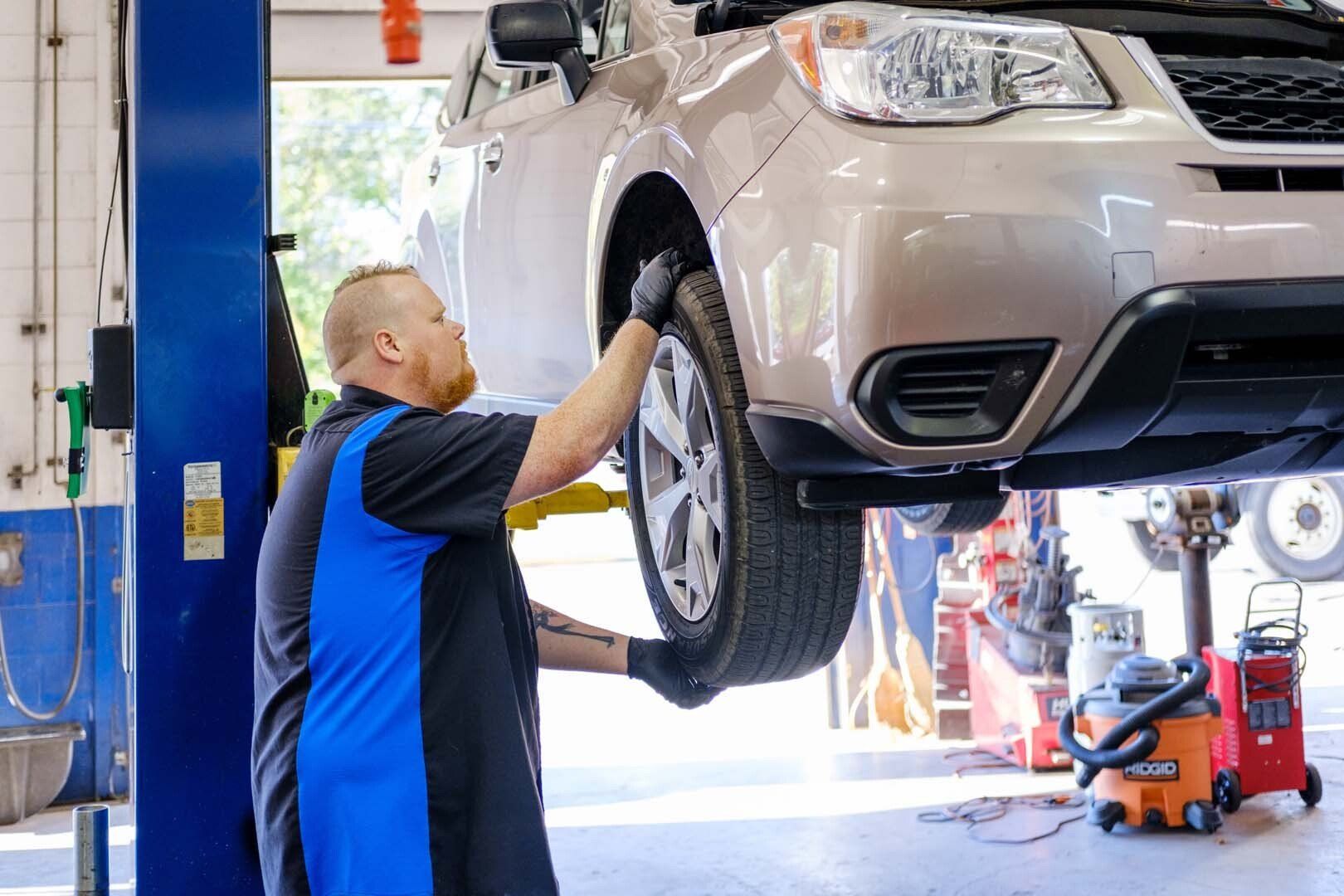 Mechanic working on a car raised on a lift in a repair shop.