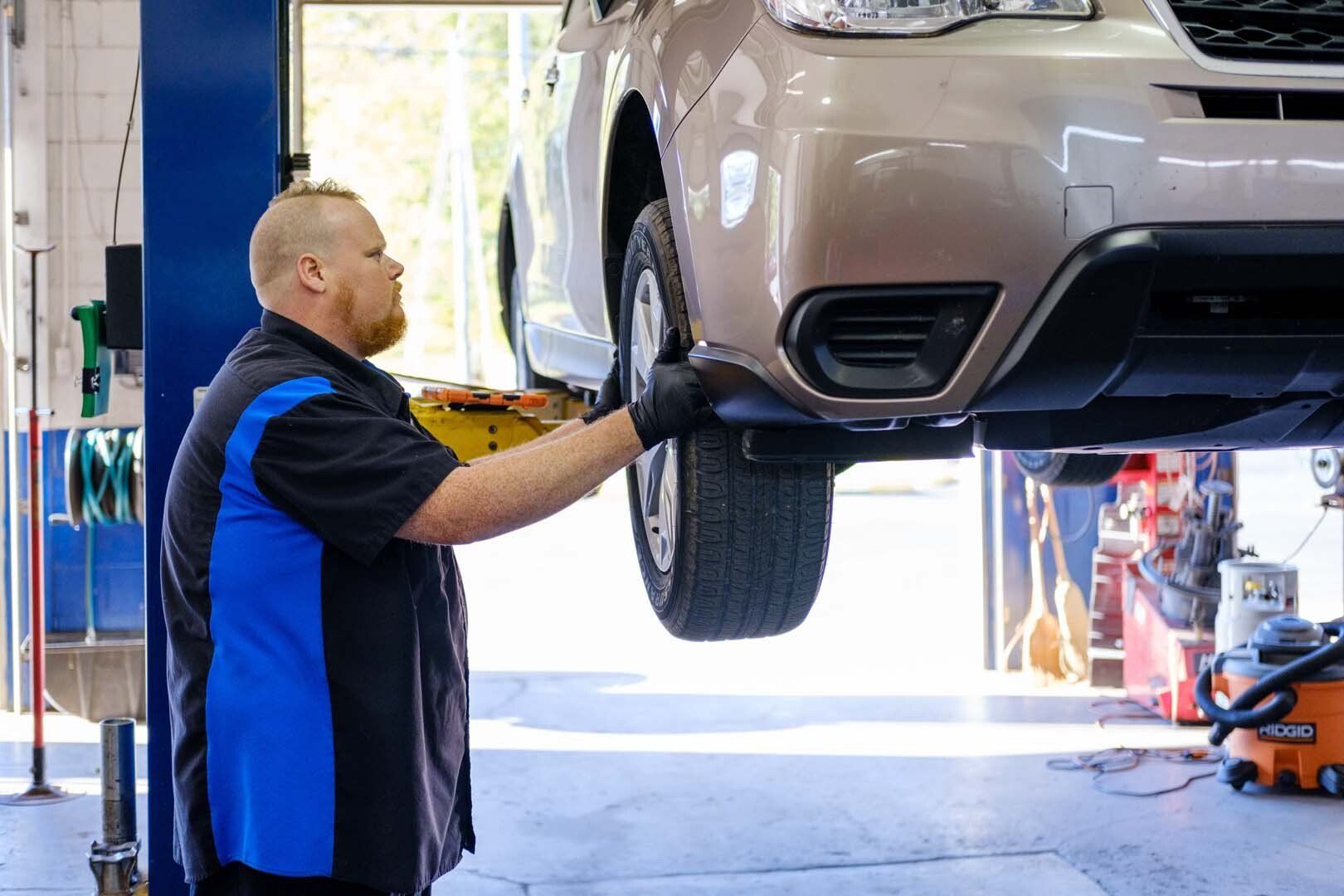 Mechanic inspecting car tire on a lift in a repair shop.