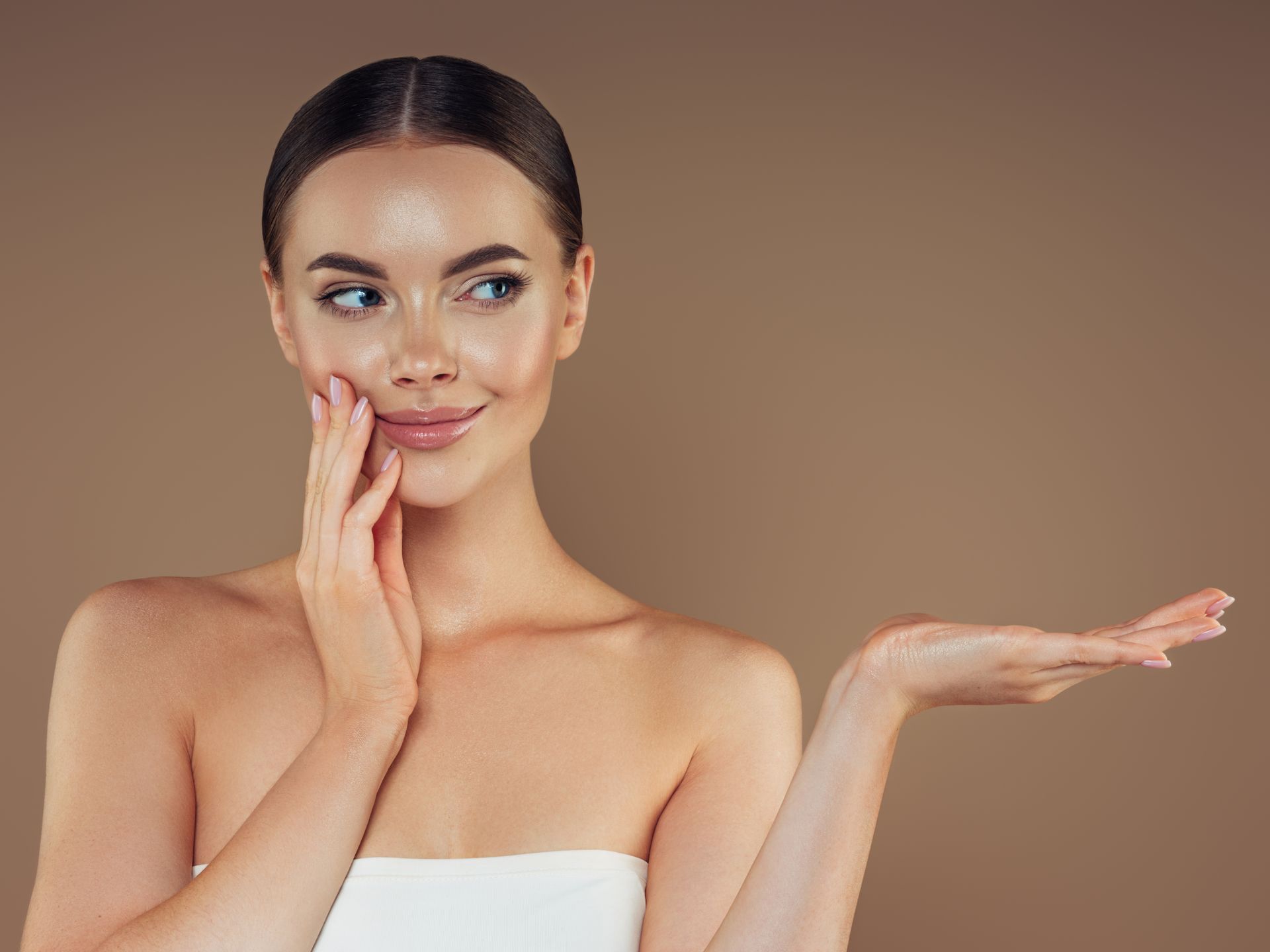 Donna dalla pelle chiara, sorridente, che si tiene il viso con una mano, palmo aperto rivolto verso l'alto, sfondo neutro.