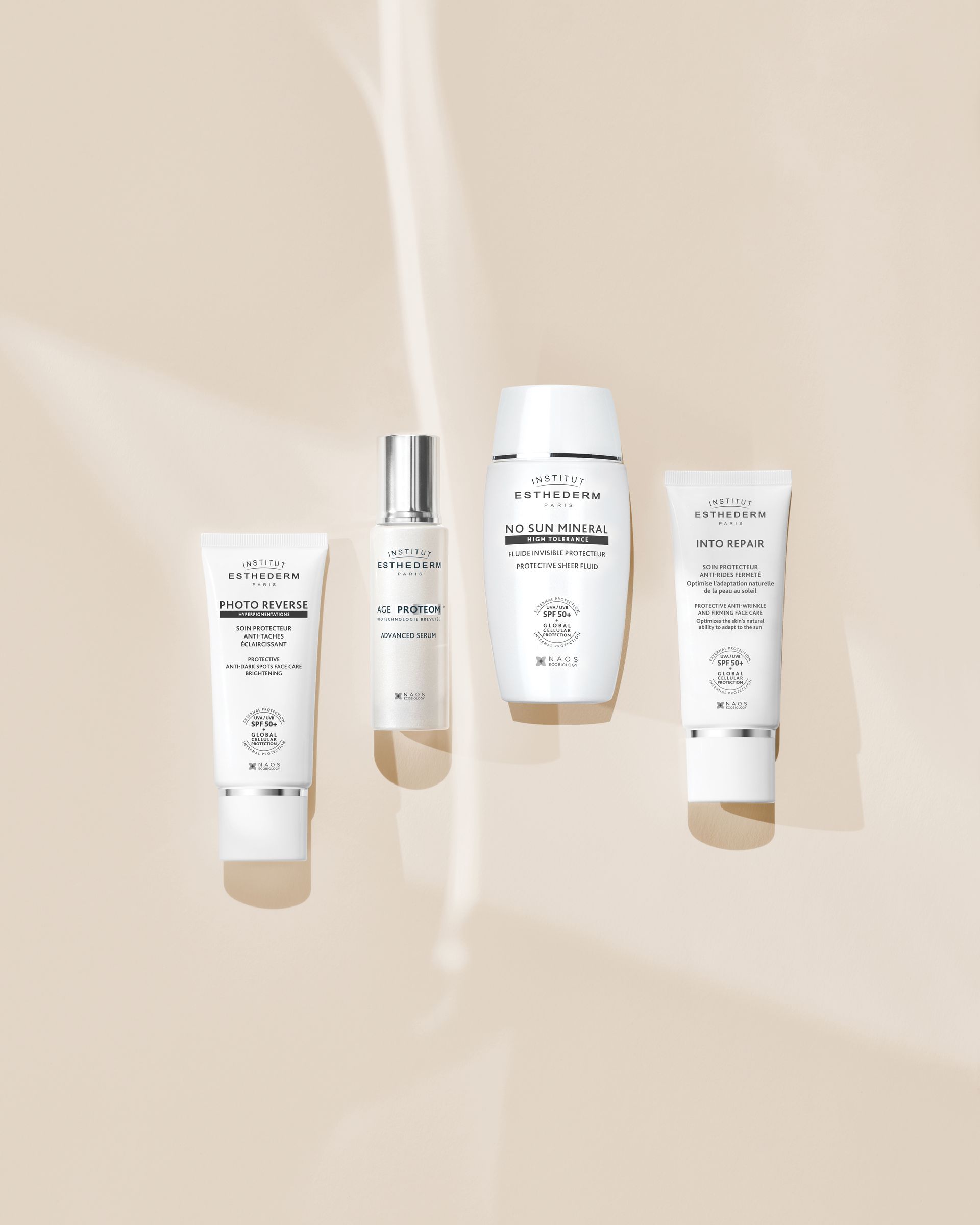 Quattro flaconi bianchi di prodotti per la cura della pelle disposti su uno sfondo neutro.