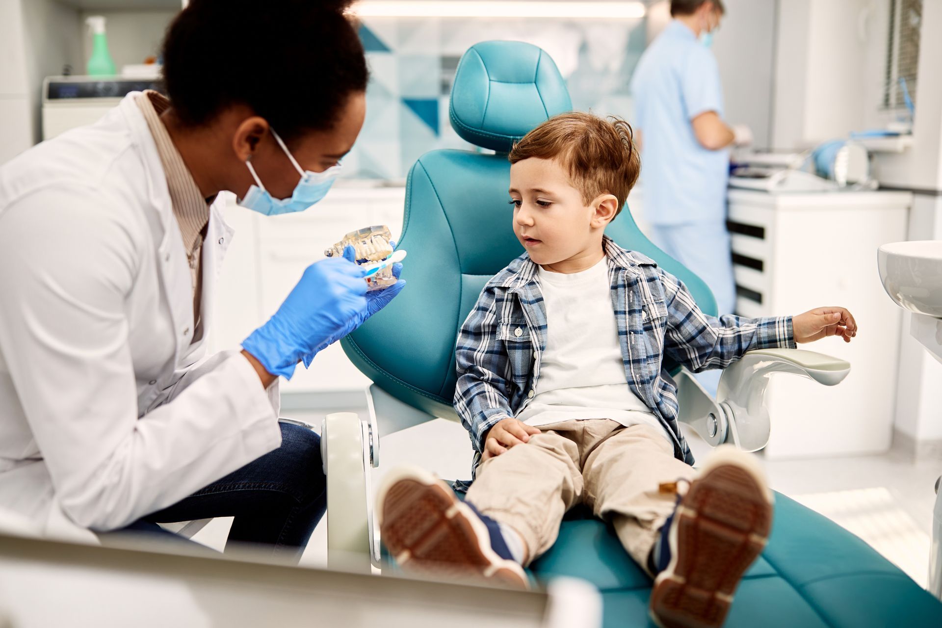 A young boy is sitting in a dental chair while a dentist examines his teeth.