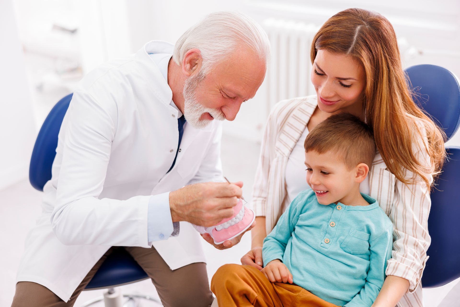 A woman and a child are sitting in a dental chair while a dentist examines their teeth.