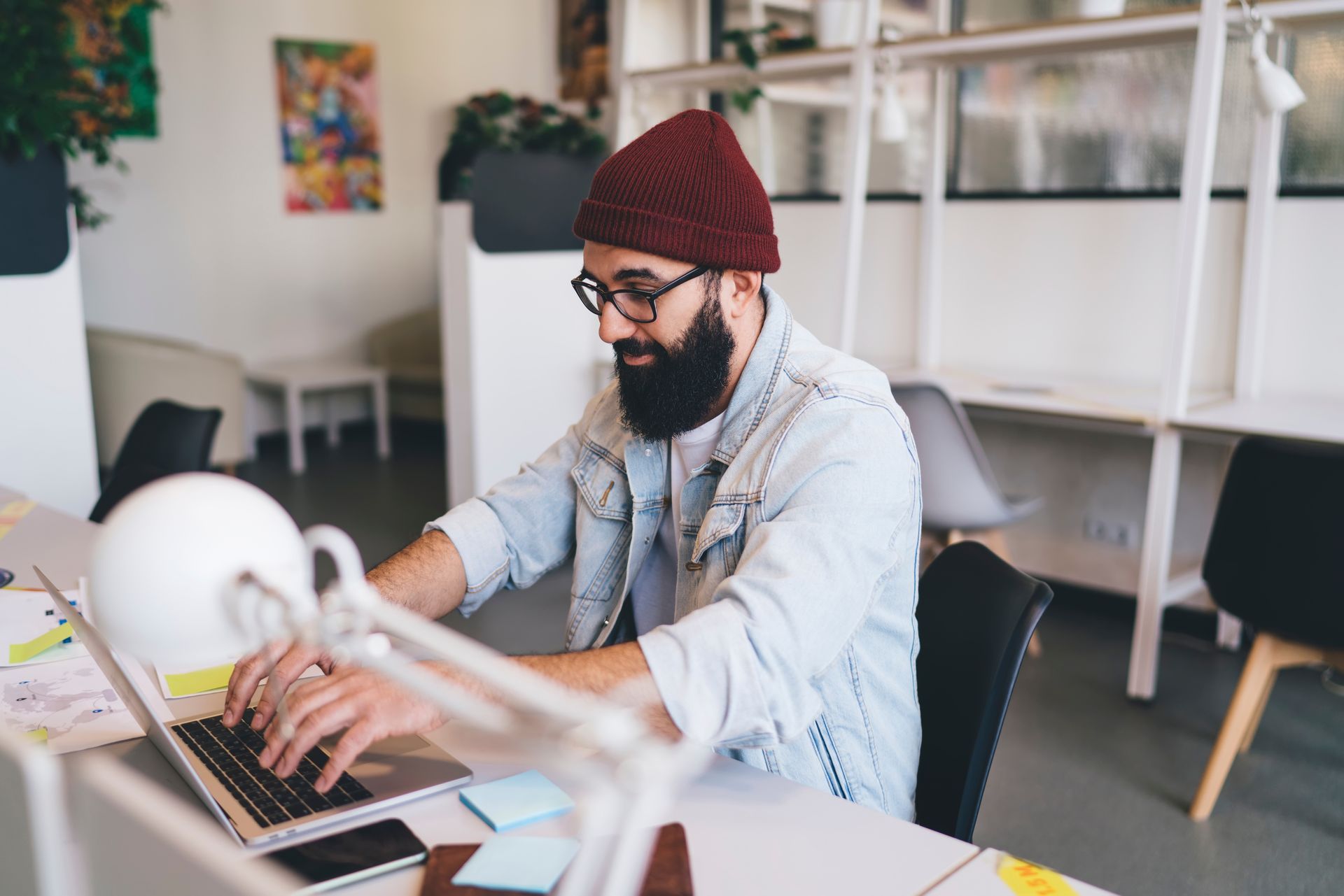 A man with a beard is sitting at a desk using a laptop computer.