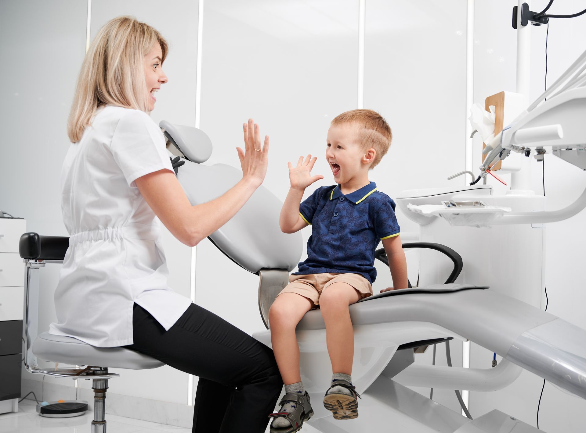 A woman is giving a child a high five while sitting in a dental chair.