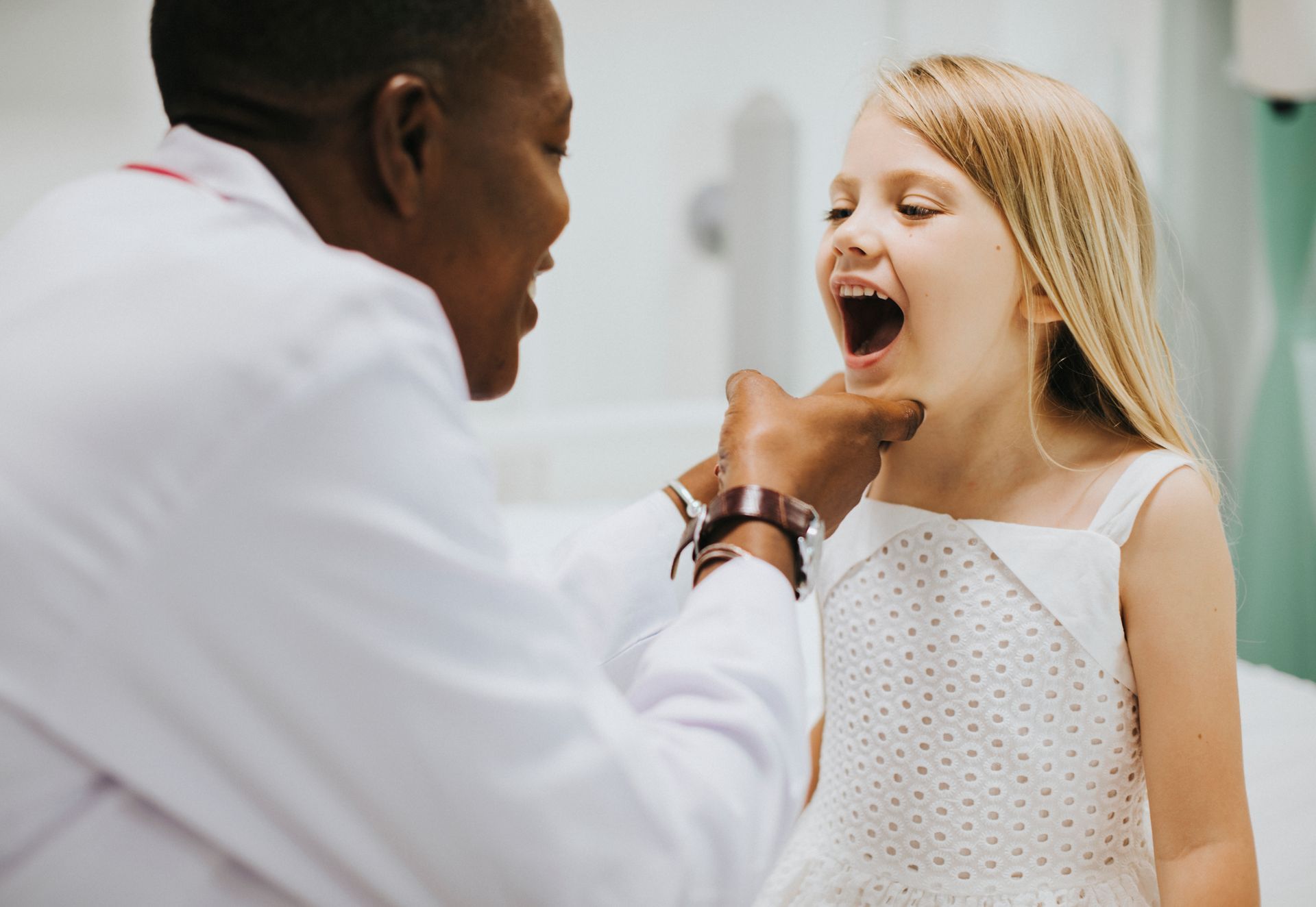 A little girl is having her throat examined by a doctor.