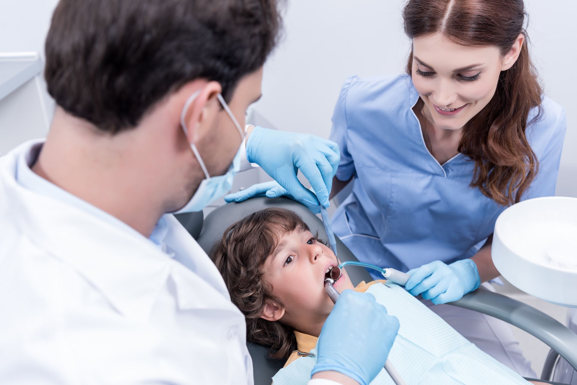 A little boy is sitting in a dental chair getting his teeth examined by a dentist and a nurse.