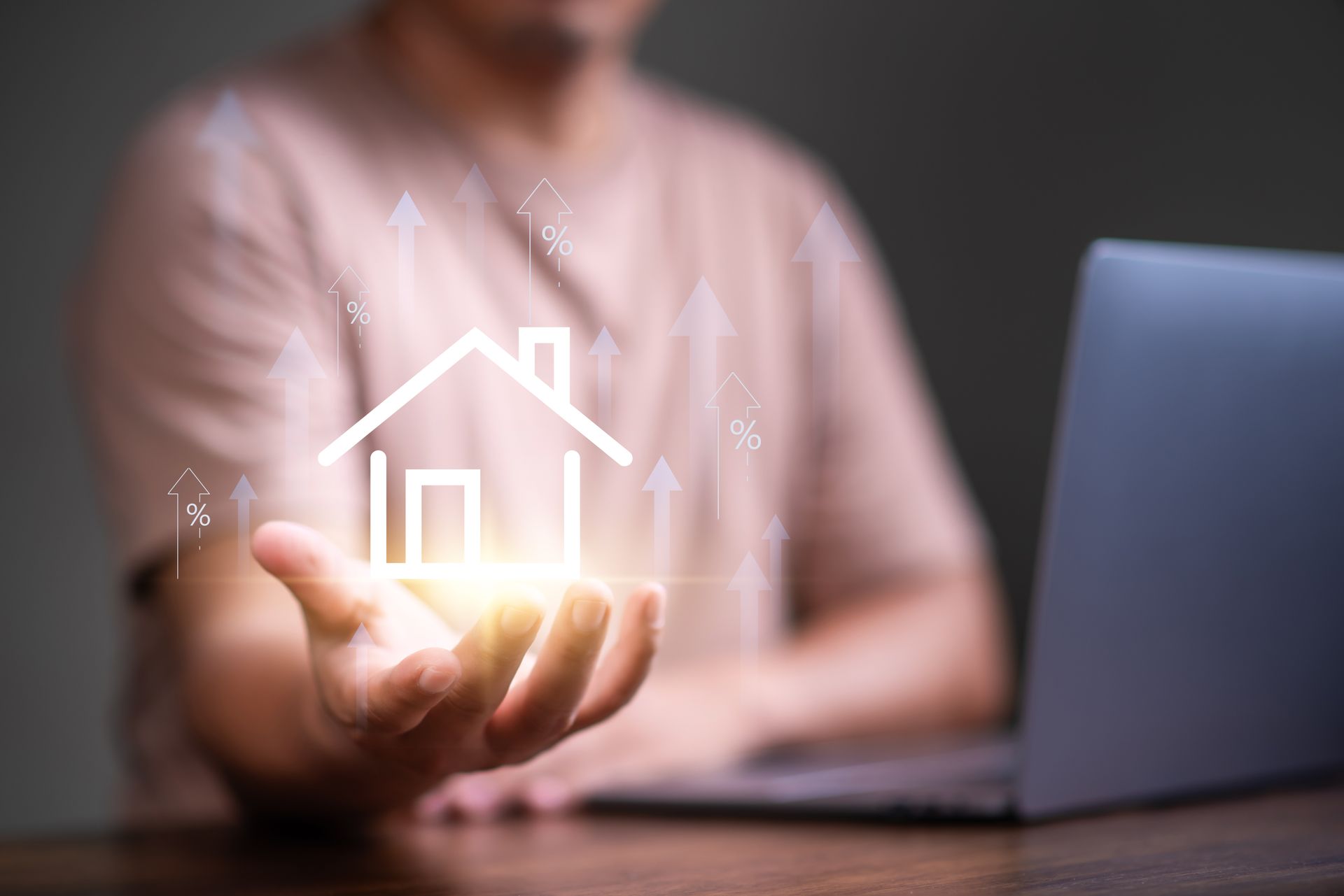 Person holding glowing house icon, laptop visible. Upward-pointing arrows suggest growth.