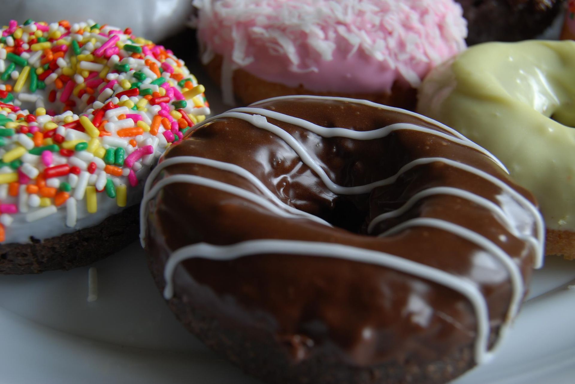 Close-up of donuts with colorful sprinkles, chocolate glaze, pink icing, and white icing.