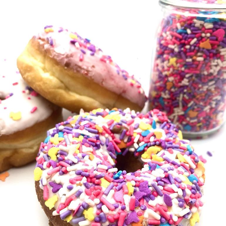Donuts with colorful sprinkles, next to a jar filled with sprinkles.