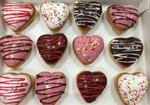 Heart-shaped donuts in a box. Various colors, icing, and sprinkles.