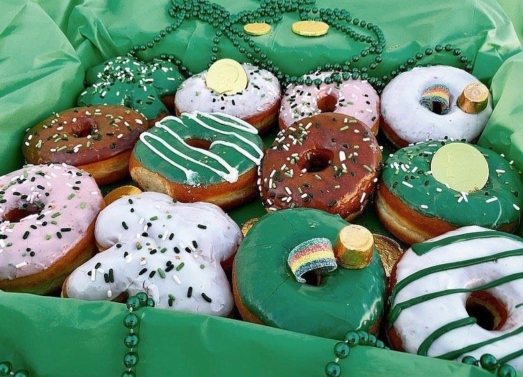 Box of St. Patrick's Day donuts with green, pink, and chocolate frosting, and shamrock sprinkles.