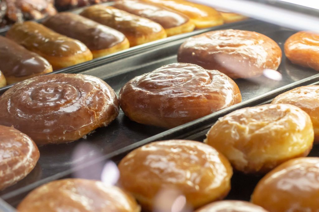 Donuts in a glass display case; various glazed and iced, golden brown and chocolate.