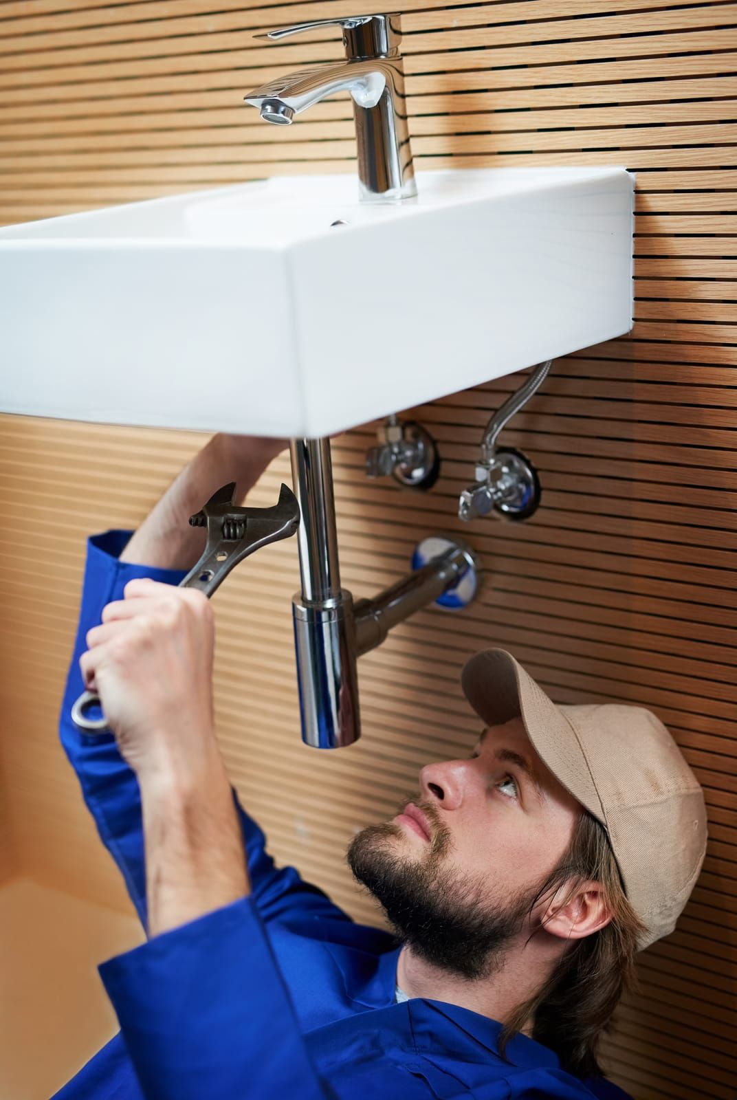 A man is fixing a sink with a wrench.