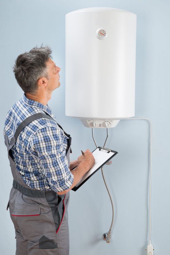A man is standing next to a water heater and writing on a clipboard.