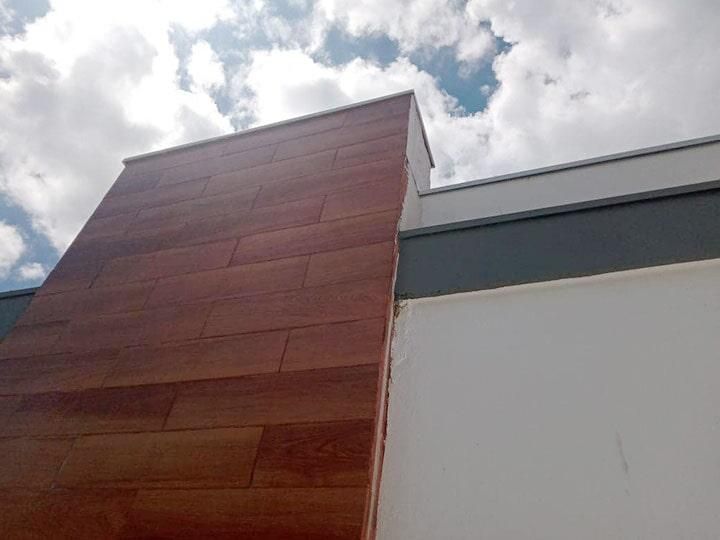 Exterior del edificio con paneles de madera y pared blanca contra un cielo nublado.