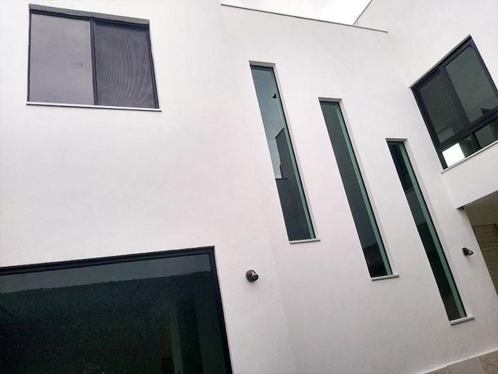 Exterior del edificio blanco con varias ventanas tintadas oscuras de diferentes formas y tamaños.