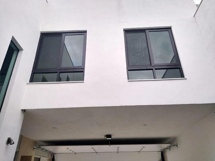 Edificio blanco con dos ventanas de marco oscuro sobre una puerta de garaje abierta.