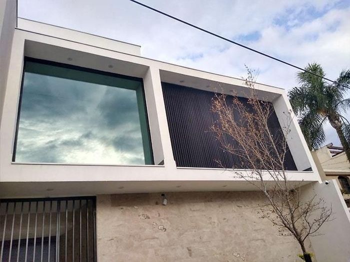 Edificio moderno blanco con gran ventanal que refleja el cielo nublado y fachada de cuadrícula negra.