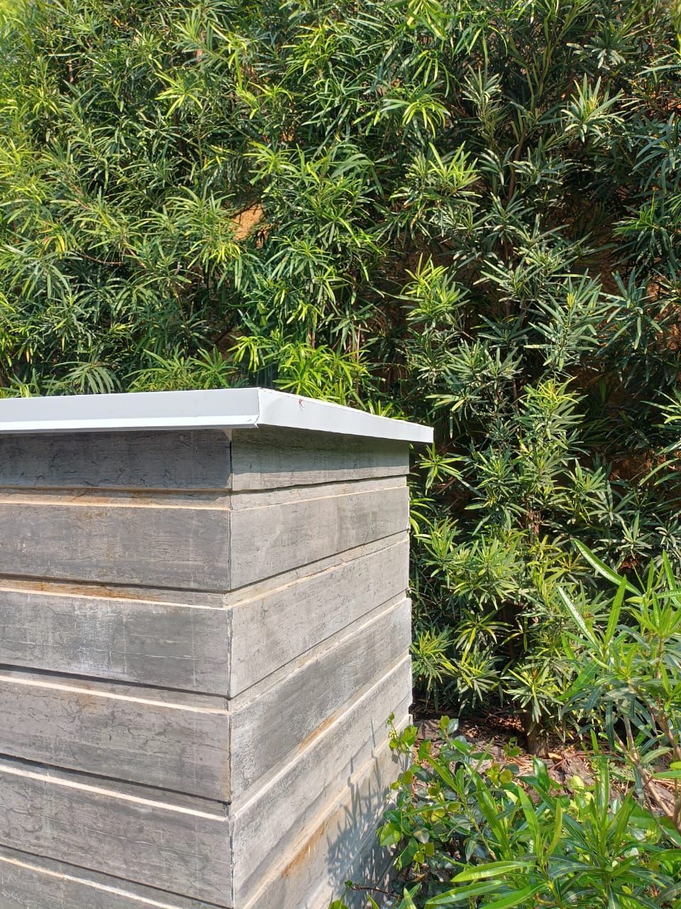 Bloques grises apilados con una capa superior blanca, junto a un frondoso arbusto verde.