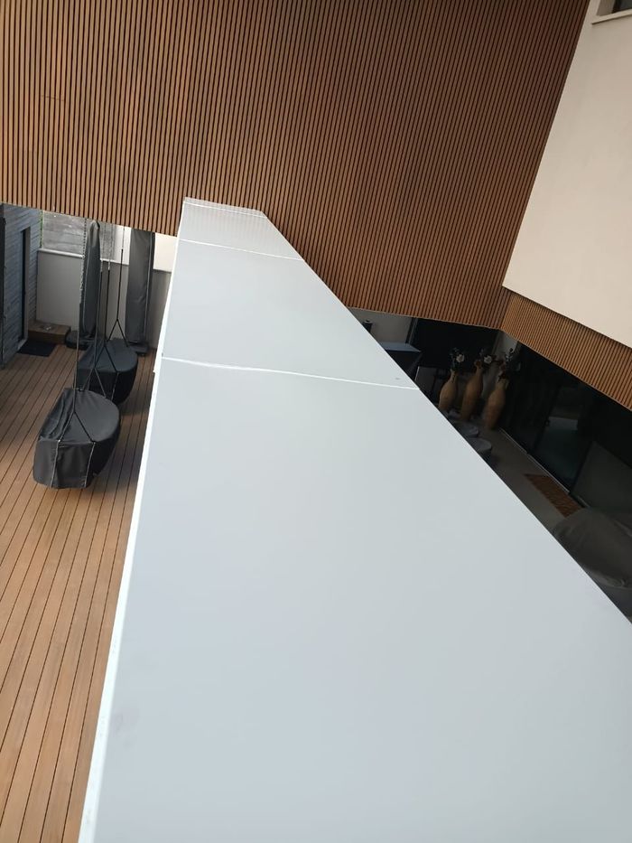 Una estructura rectangular, larga y blanca se extiende a lo ancho de la imagen. Detrás de ella, una pared de listones de madera y un espacio interior.