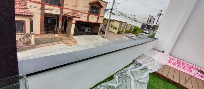 Desde un balcón se ve una calle, edificios y un atisbo de césped. El cielo está nublado.