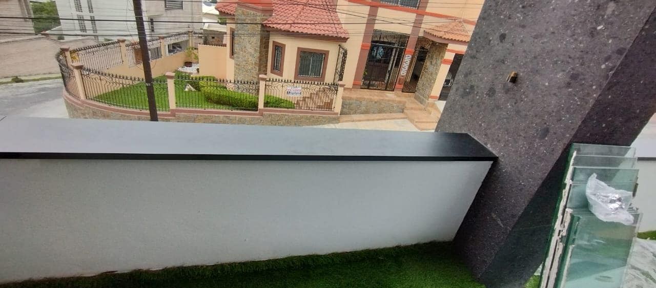 Exterior de un edificio moderno con una zona de césped y una casa al fondo.