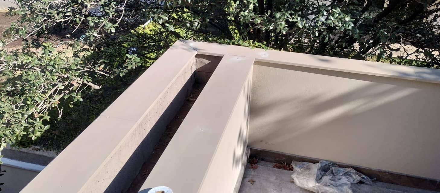 Una pared beige con un profundo canal sobre un fondo de árboles verdes y cielo.