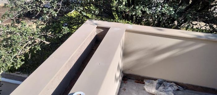 Una pared beige con un profundo canal sobre un fondo de árboles verdes y cielo.