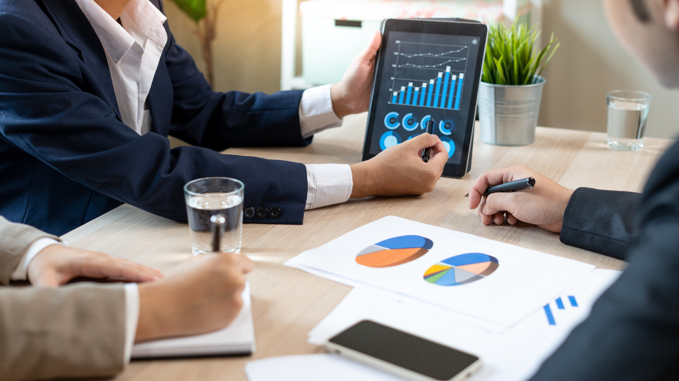 Business meeting, people reviewing data charts on tablet and paper at a table.