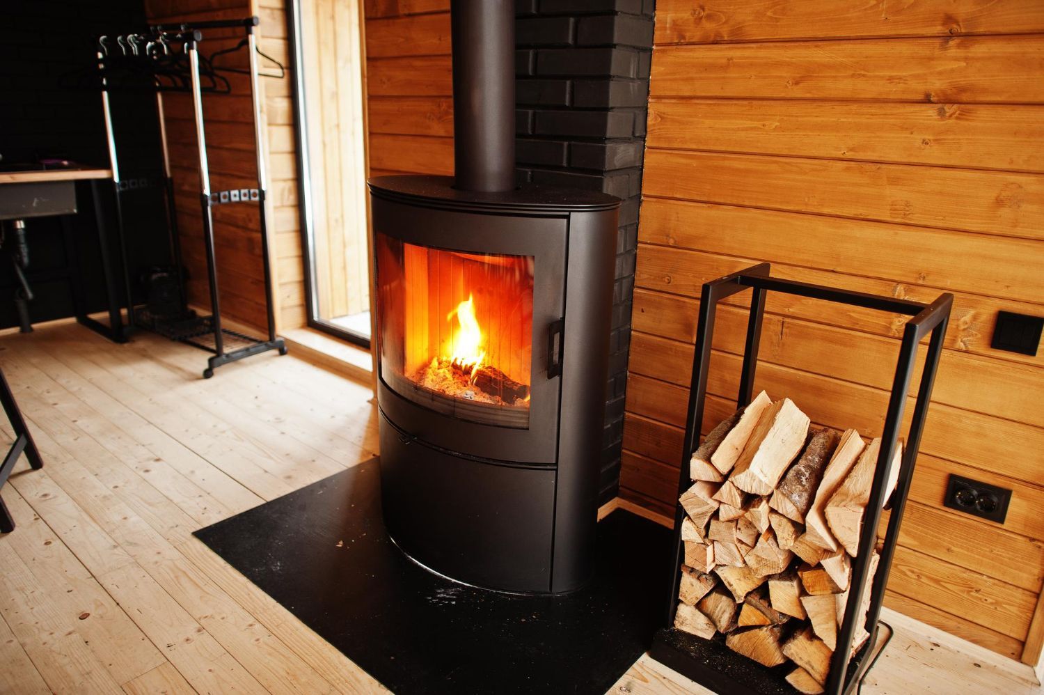 A wood stove is sitting in a wooden room next to a pile of logs.