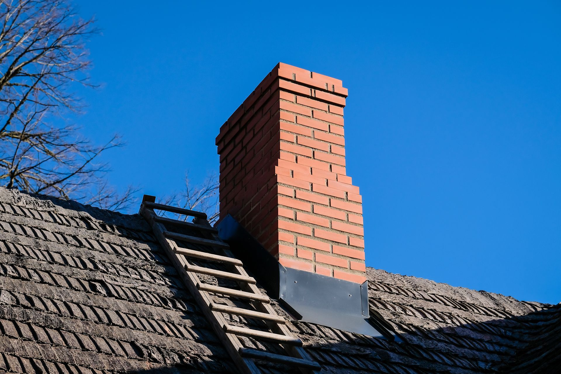 A brick chimney on top of a thatched roof with a ladder attached to it.