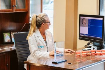 Dentist in lab coat examining computer screen at desk with dental models.