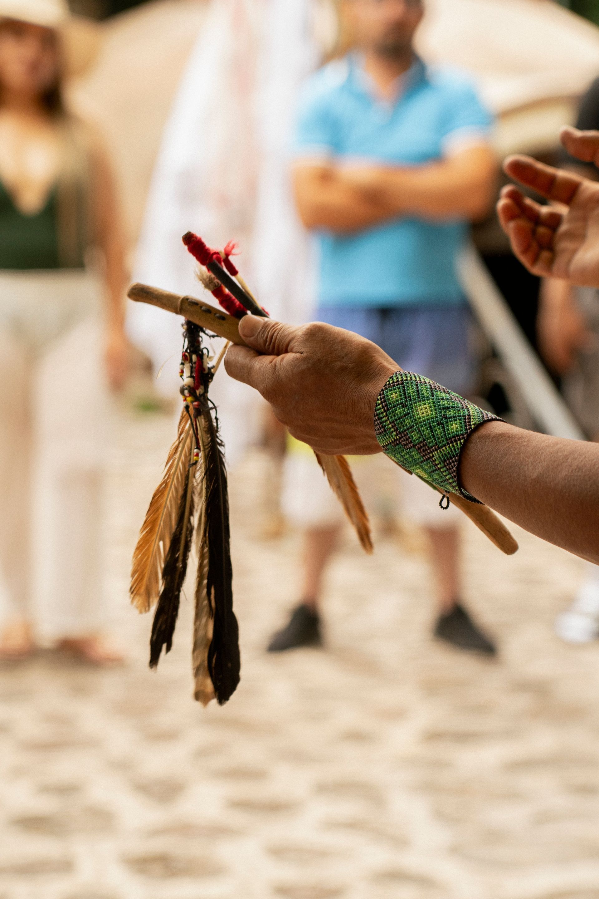 Persona sosteniendo varitas con plumas, con pulsera de cuentas, al aire libre.