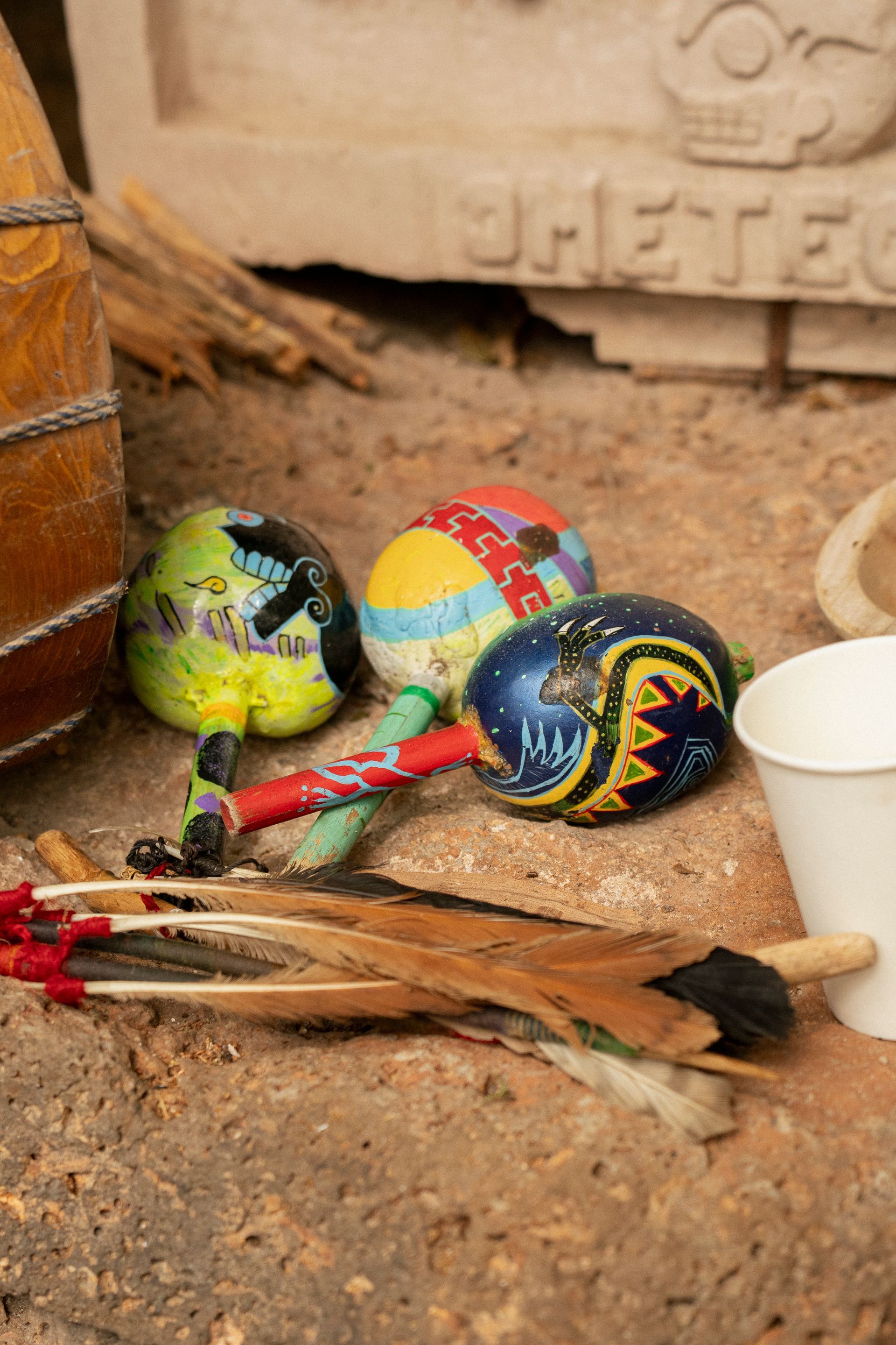 Sonajeros de calabaza pintados de colores, plumas, tambor y taza sobre una superficie de piedra.