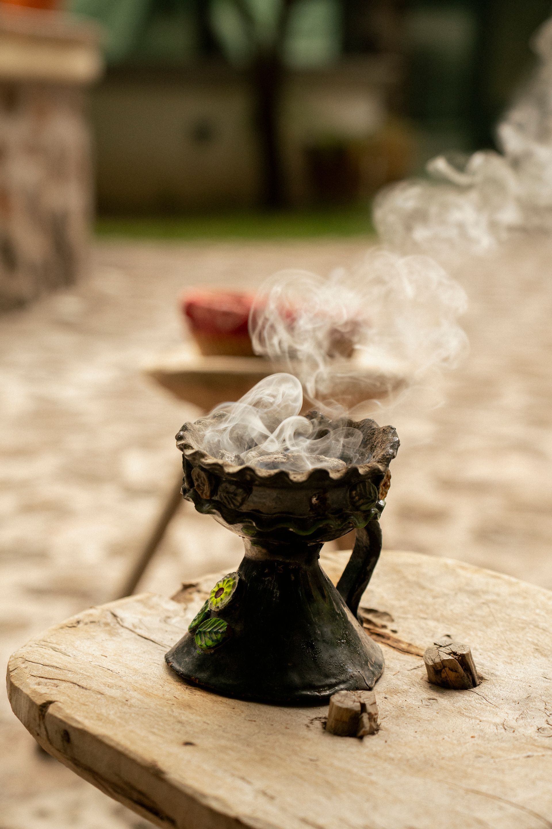 Quemador de incienso con humo denso sobre una superficie de madera al aire libre; fondo borroso.