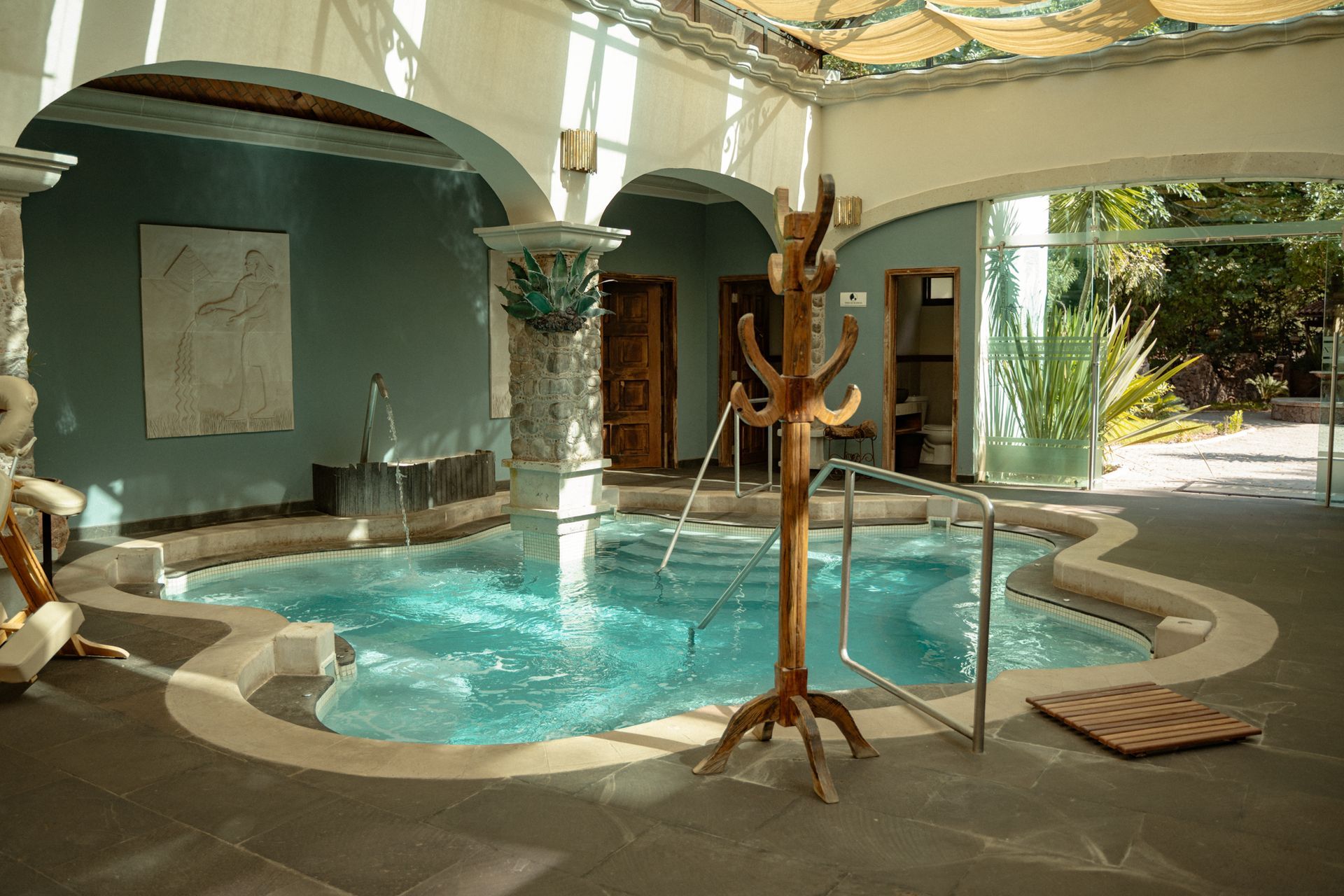 Piscina de hidromasaje interior con agua azul, rodeada de azulejos y columnas color canela.