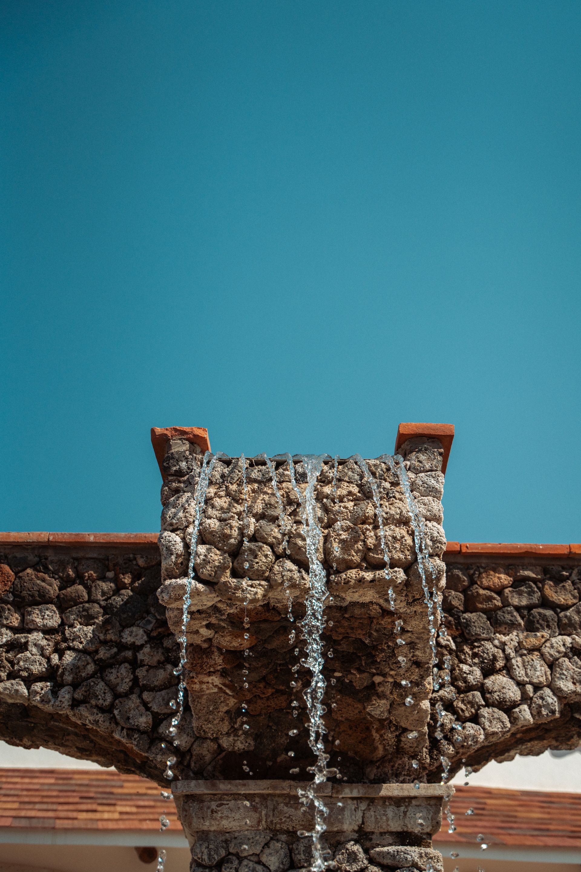 Cascada que cae en cascada sobre un arco de piedra contra un cielo azul brillante.