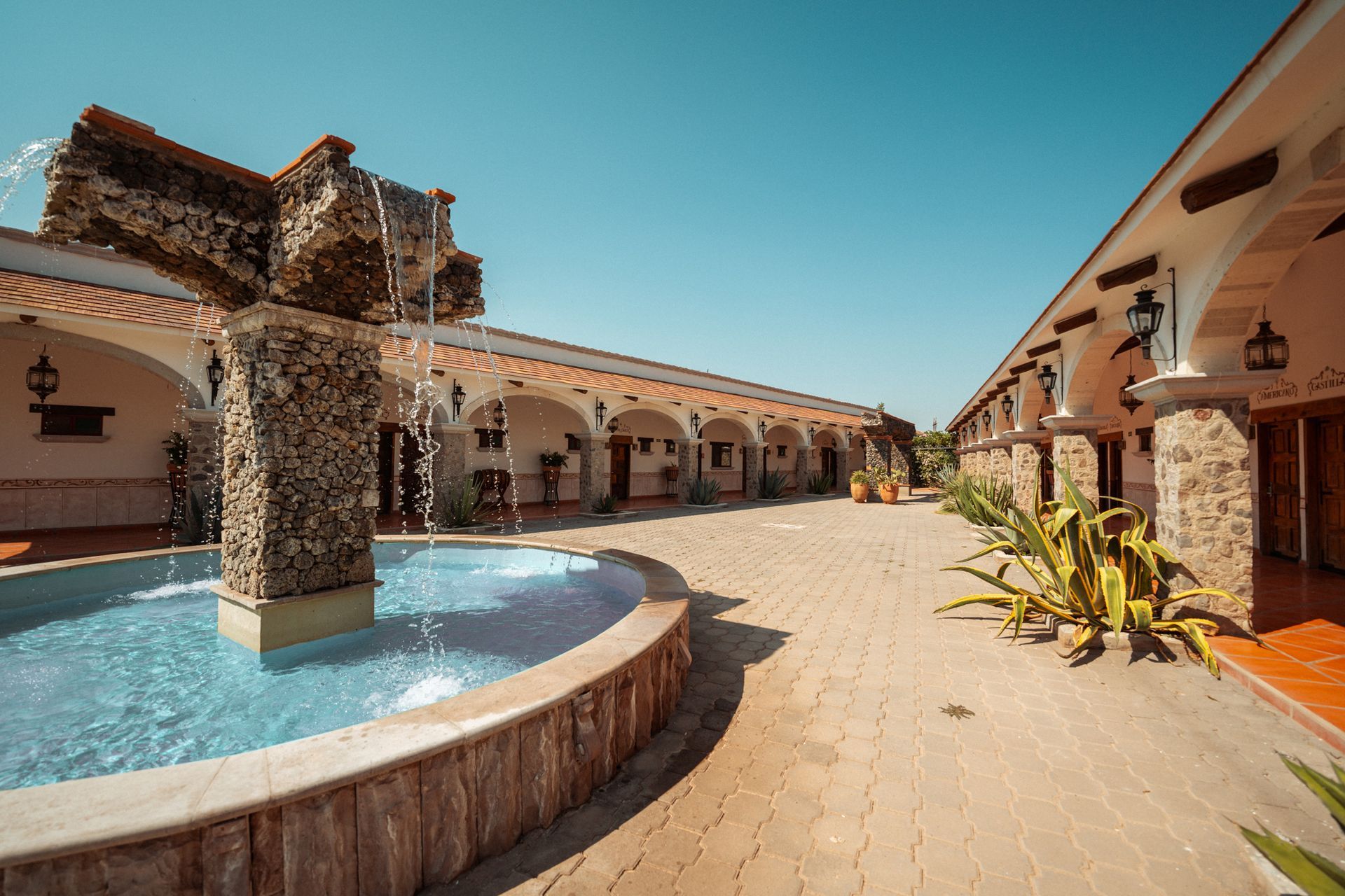 Patio con fuente, pasarelas arqueadas, columnas de piedra y cielo azul despejado.