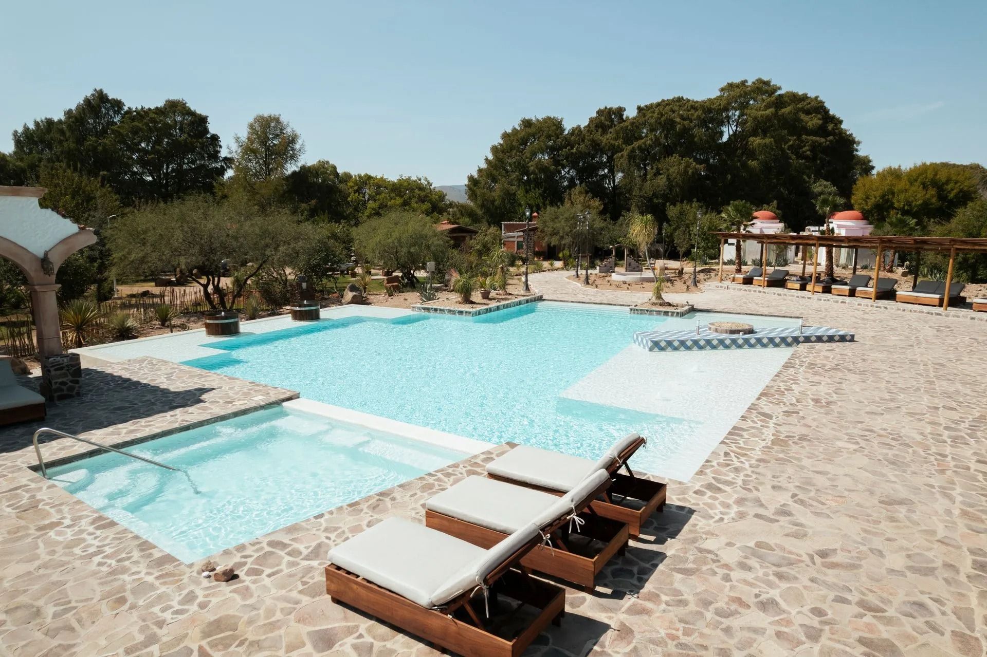 Piscina rectangular con una zona de descanso poco profunda, rodeada por una terraza de piedra con camastros.