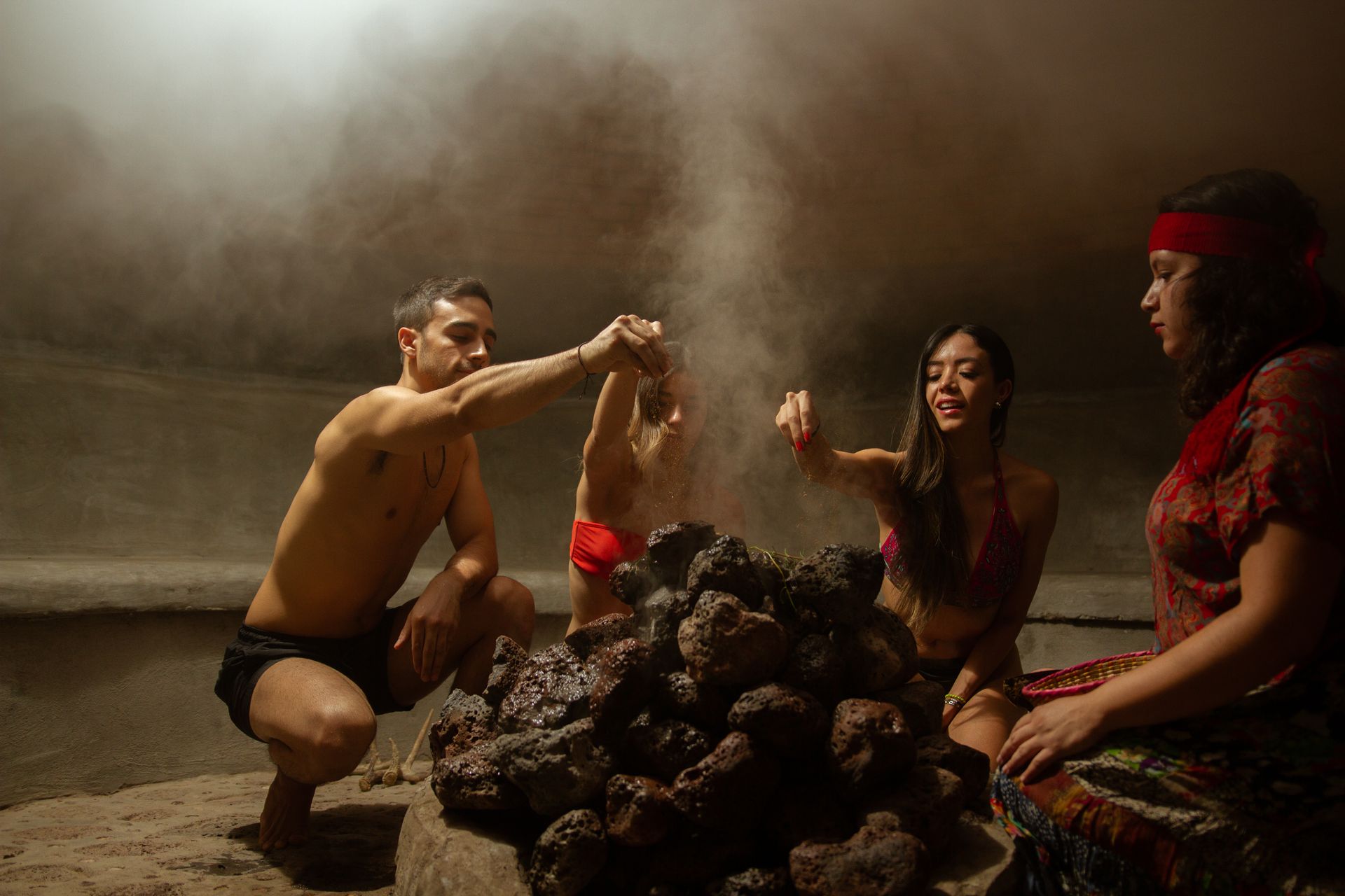 Varias personas se encuentran cerca de un montón de piedras calientes en un espacio oscuro y lleno de humo.