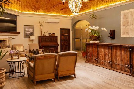 Warm-toned living room with a bar, piano, and seating. Ornate ceiling and wooden accents.