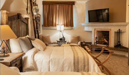 Bedroom with a king-size bed, fireplace, TV, sitting area, and wooden accents. Beige and brown color scheme.