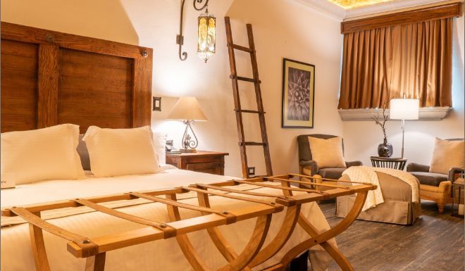 Bedroom with a large wooden bed, luggage rack, and two armchairs.