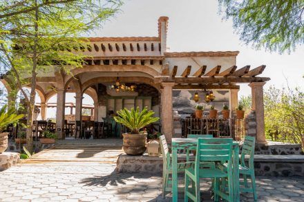 Outdoor restaurant with turquoise chairs, stone columns, and overhead wooden beams.
